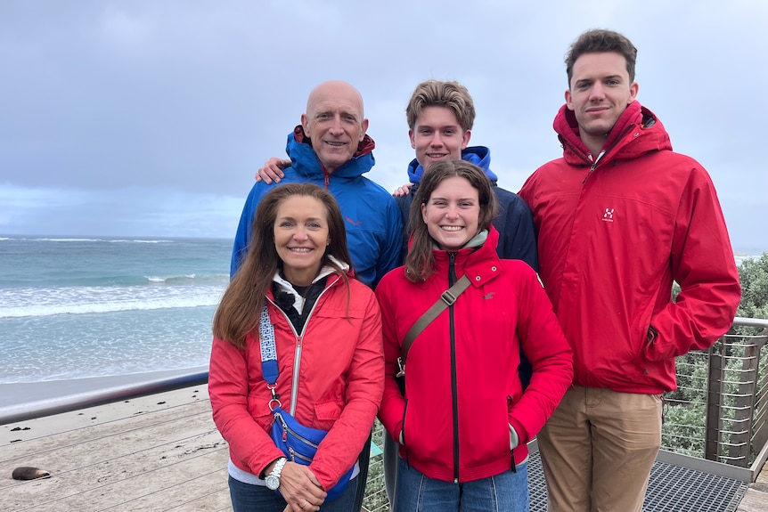 Five people in zipped up wind jackets standing on a viewing platform of a boardwalk that over looks a beach.