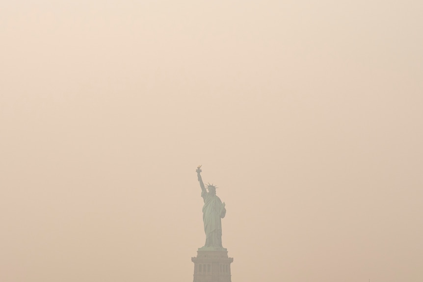 The Statue of Liberty is just visible through a hazy sky, which is tinged with a yellow colour.