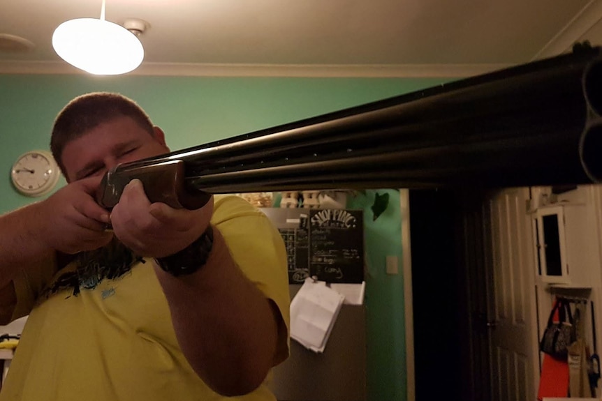 An Australian man wearing a yellow shirt and holding a gun.