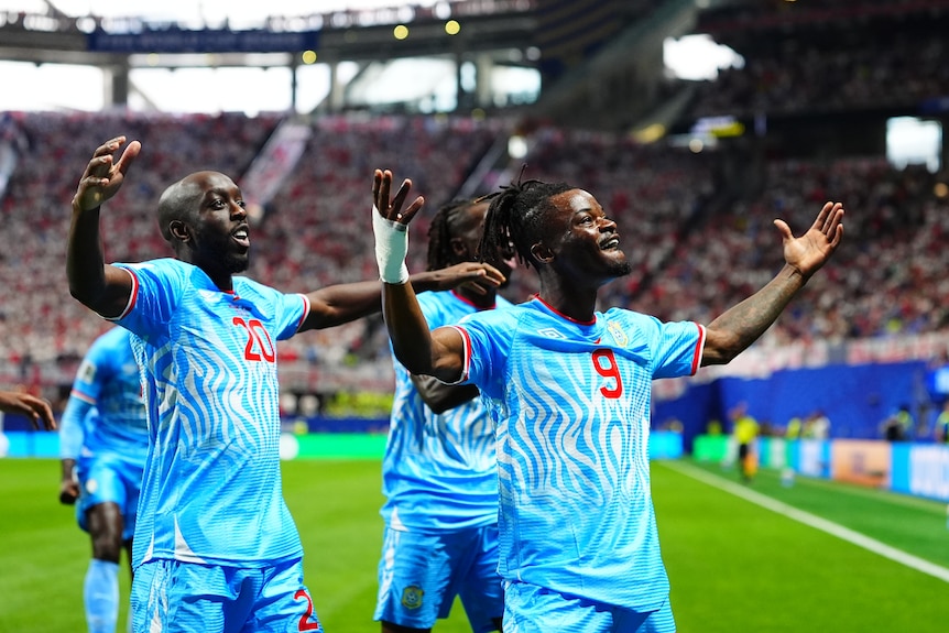 Two soccer players in blue have their arms outstretched in celebration of a goal