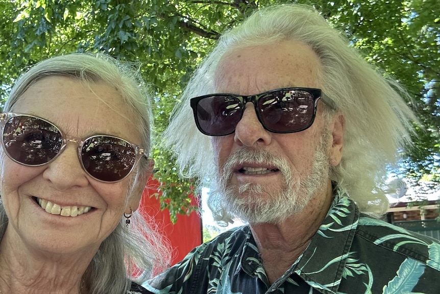 A man and woman in their 70s smile at the camera while wearing sunglasses