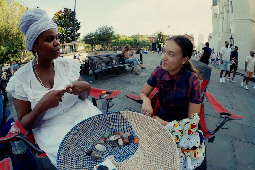 Mikaela sits and talks to a fortune teller on the street.