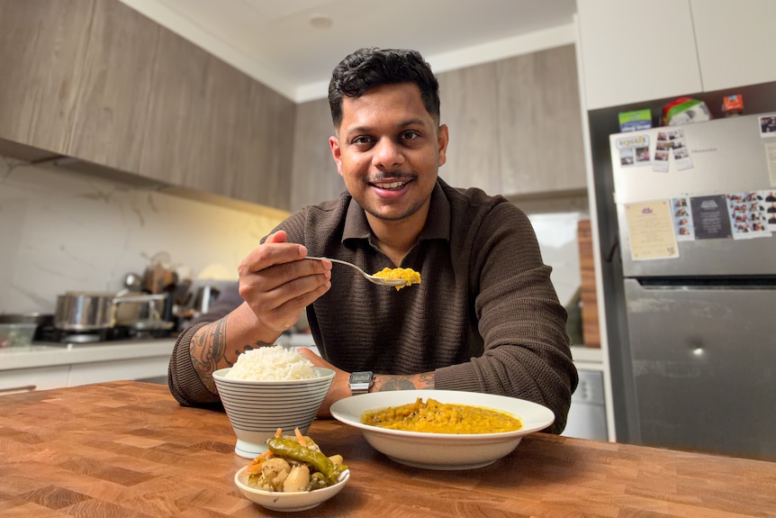Nip Liyanapathirana sits behind a bowl of his dal, holding a spoonful and smiling.