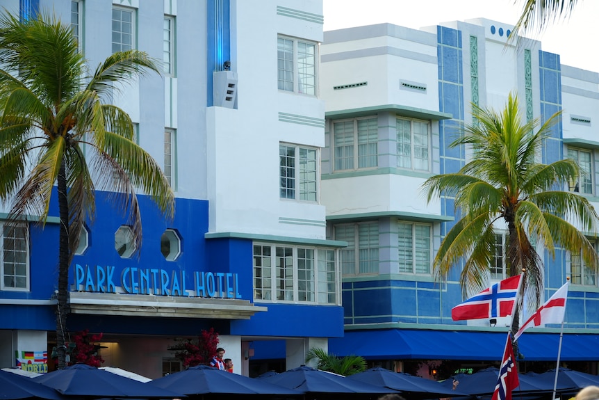 A blue and white art deco building with a Norway and England flag flying in foreground.