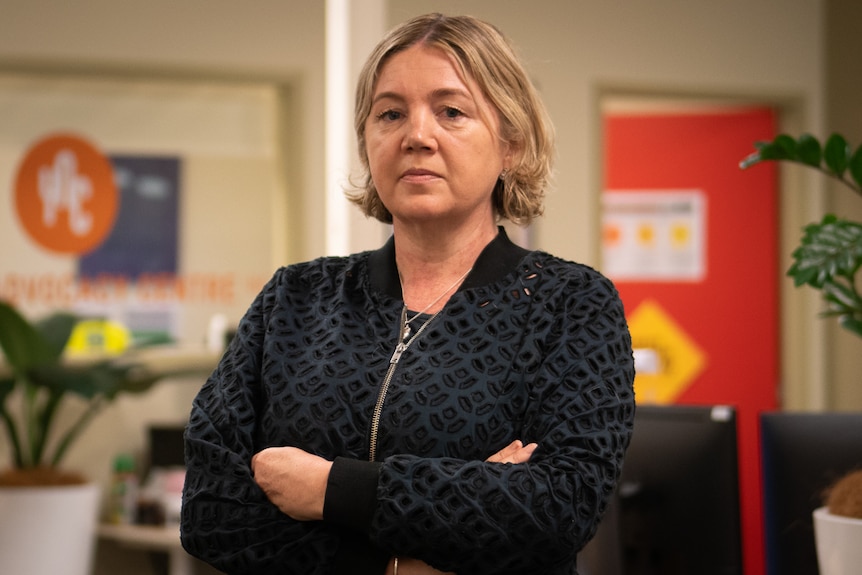 A woman stands with her arms folded in an office