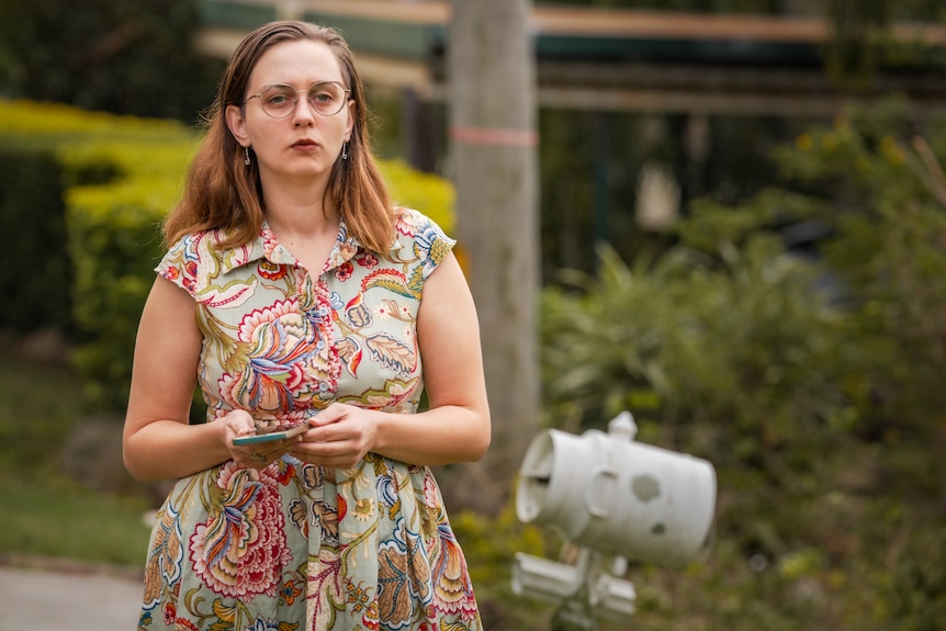 A woman stands on a suburban street holding her phone
