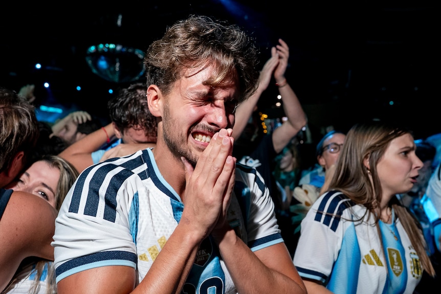 A man in an Argentina jersey clasps hands and cries with joy.