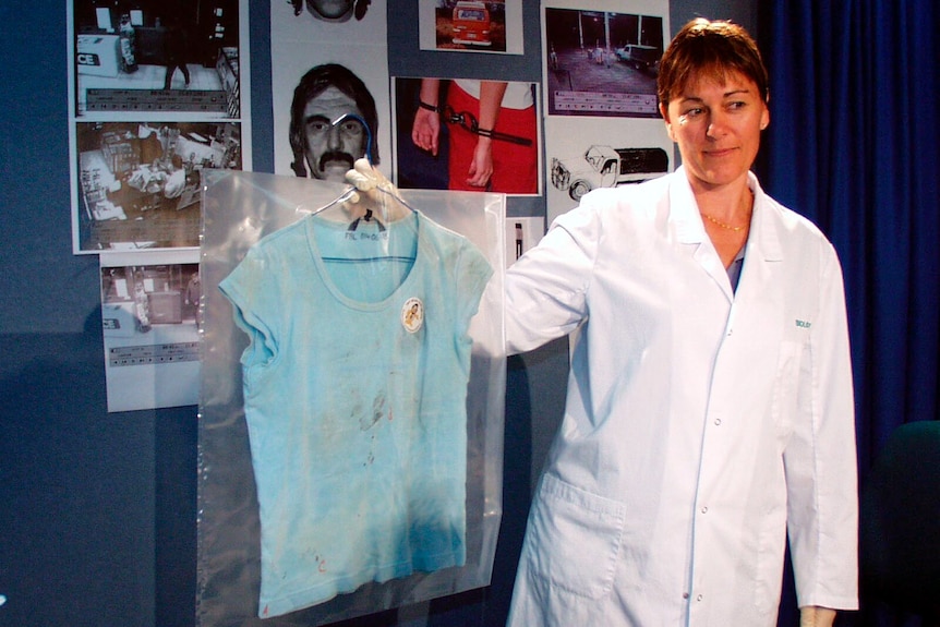 A biologist in a lab coat holding a shirt with blood stains on it.