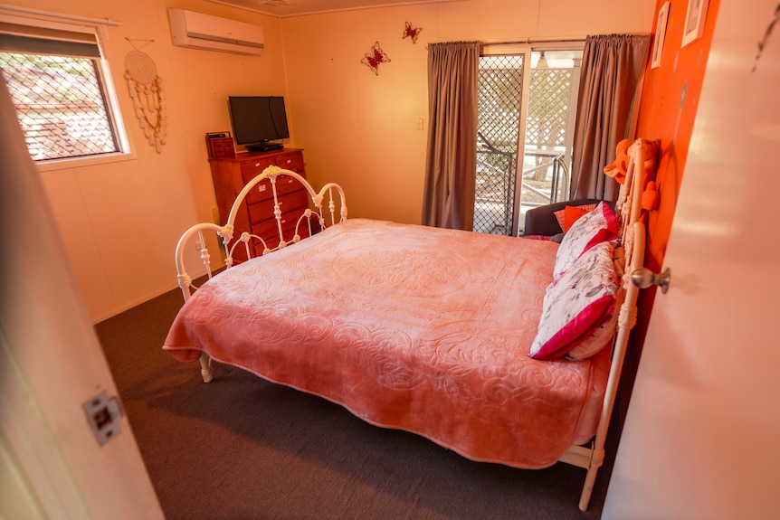 A bed with a pink quilt in a bedroom with an orange wall.