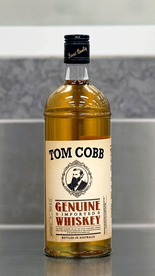 A bottle of Tom Cobb whiskey on a metal bench.