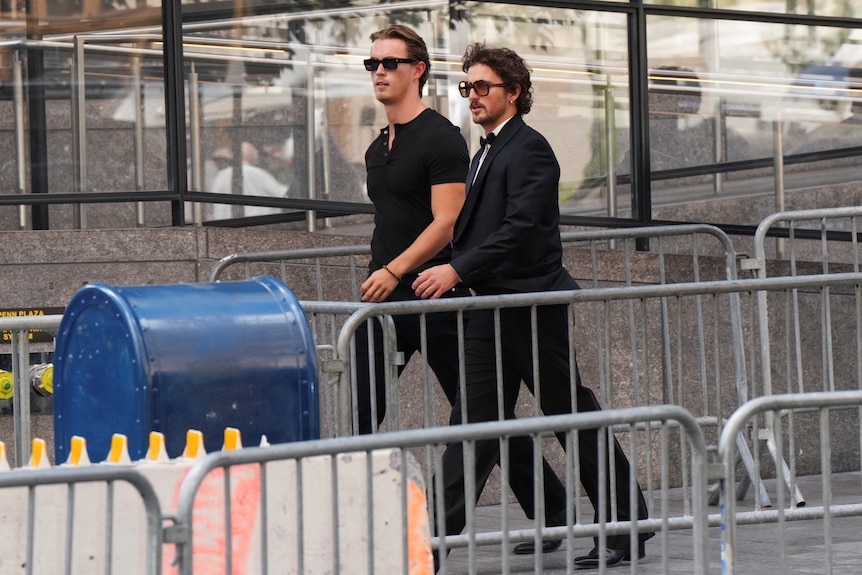 Two men in blac walk past barricades.