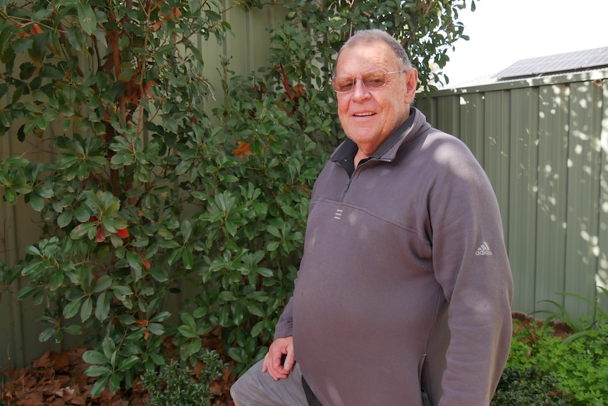 A man in a grey jumper standing in front of a fence.