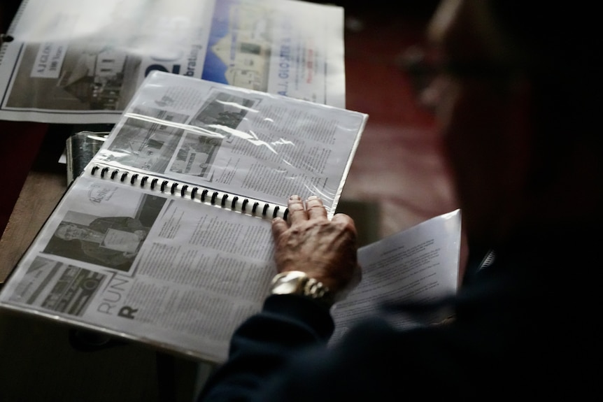 Moody photo overlooking a man's shoulder as he flicks through a display book of historic black and white photos of family