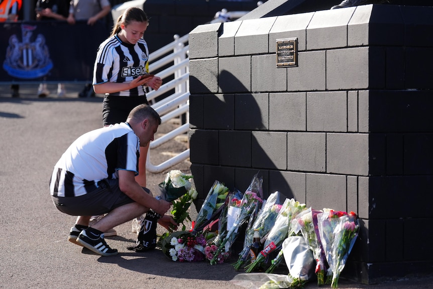 A man and a woman in black-and-white striped football shirts lay flowers atthe base of a statue.