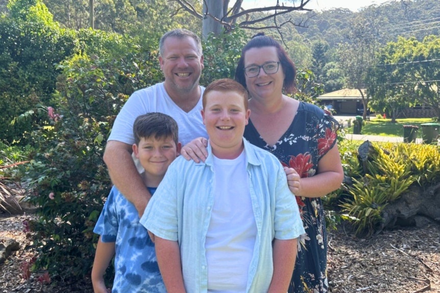 A man and woman stand with two boys in front of them, there is a garden in the background.