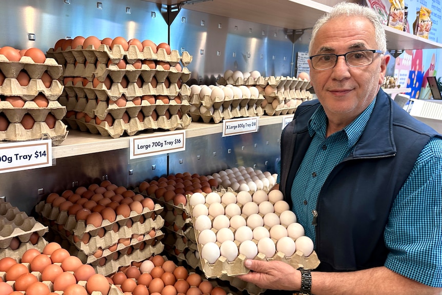 Image of an older man with pallets of eggs in cartons in hands.