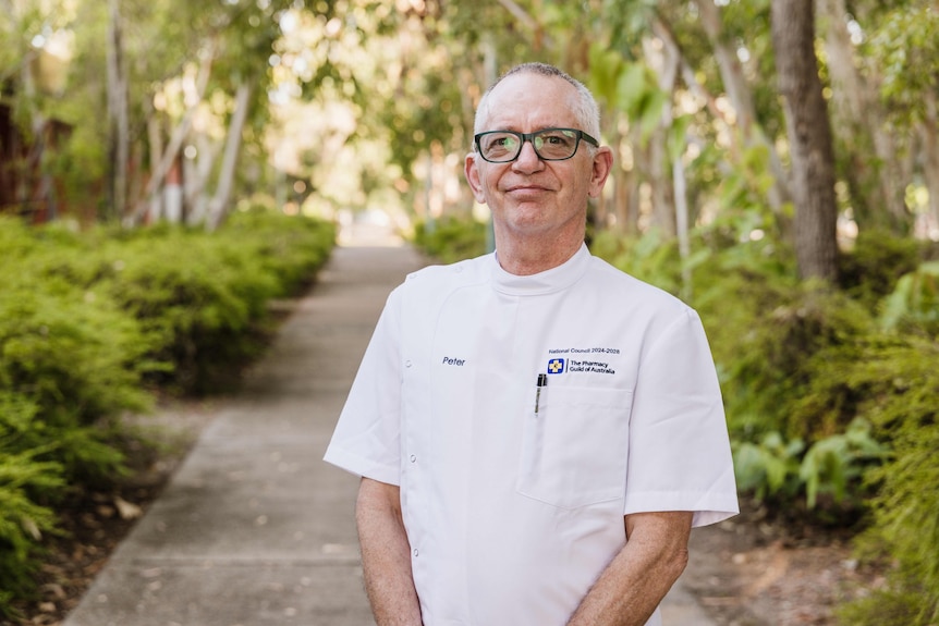A man wearing a white chemist shirt smiles at the camera.