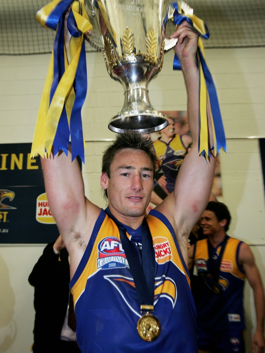 Man in AFL singlet holds up trophy