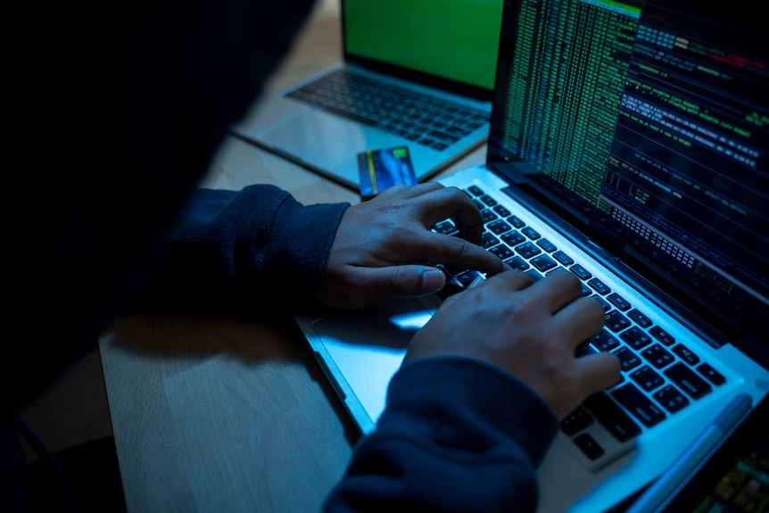 A dark image of a person's hands at a laptop