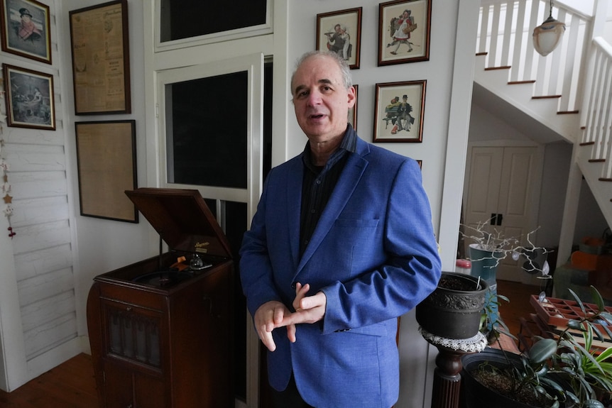 a man in his living room, speaking while looking at the camera