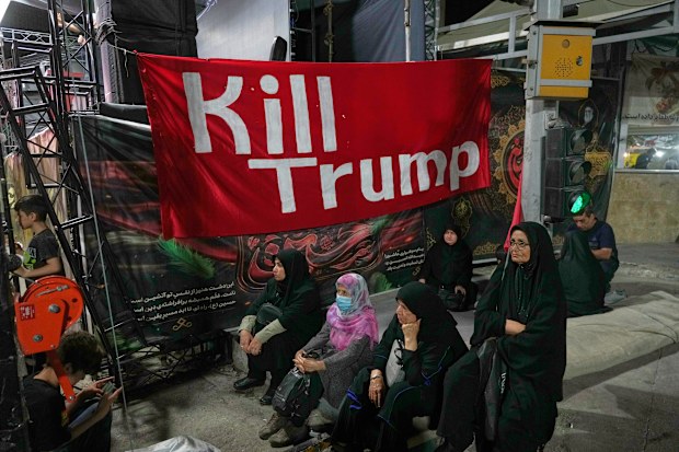 Women sit beneath a banner reading in English, “Kill Trump,” during a pro-government rally in Tehran.