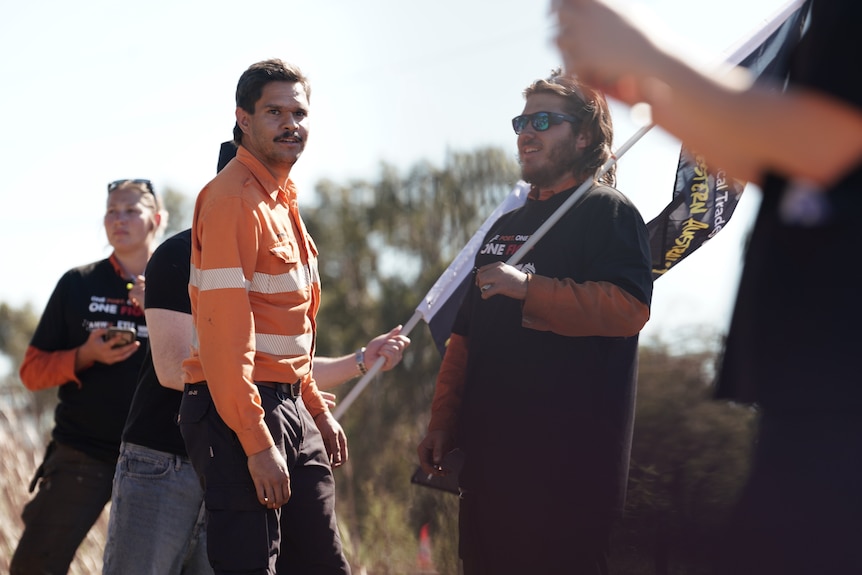 A man in an orange unofrm stands in front of people holding flags.