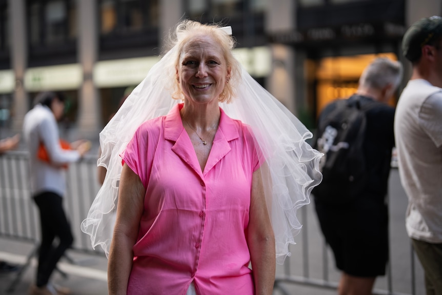 A woman wearing a veil and a pink shirt stands on a street near Madison Square Garden.