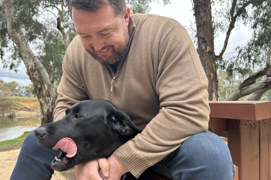 A man smiles over his dog's head