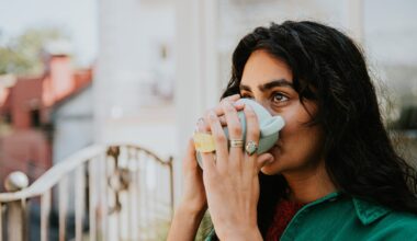 A woman cups her hands around a mug and drinks the brew