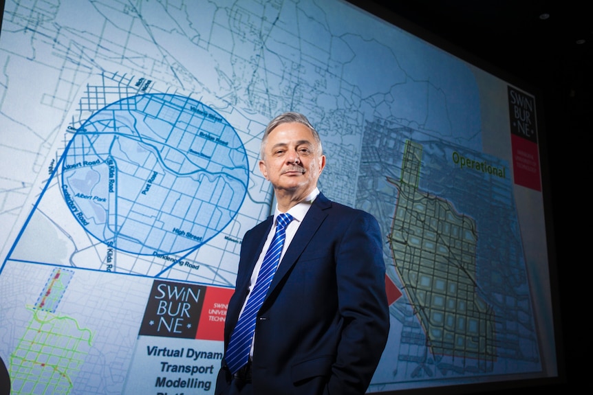 A photo of a man in a navy suit standing in front of a road network map with the Swinburne University logo.