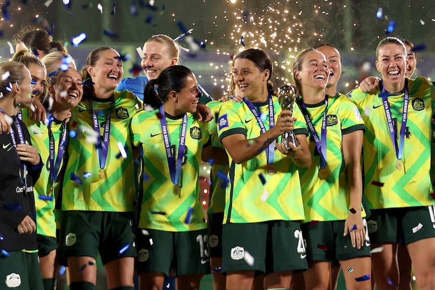Female football players on the podium, captain in centre lifting trophy