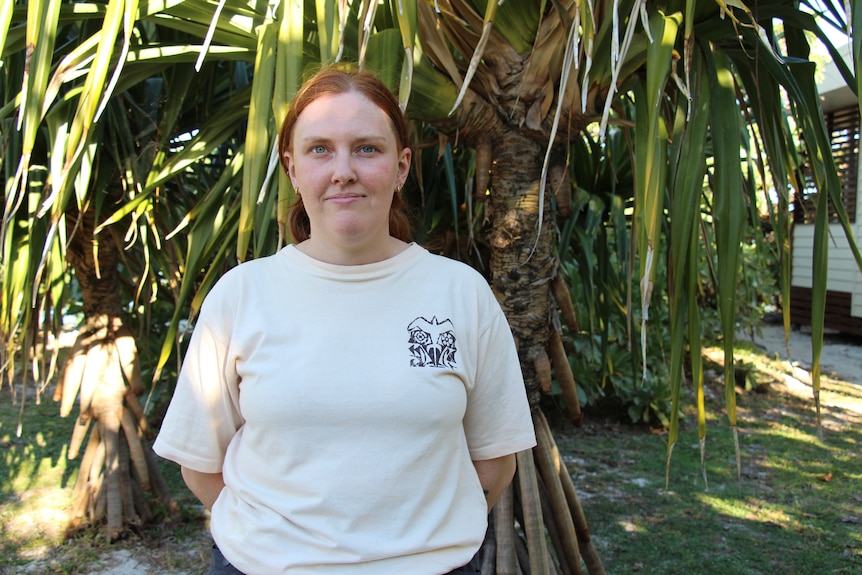 A young woman with red hair tied back and standing in front of a pandanus tree