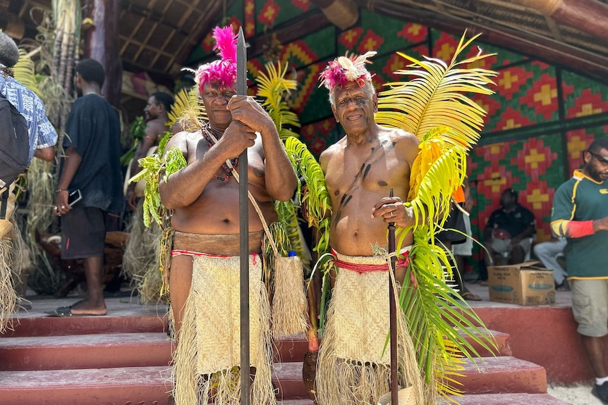 Two Vanuatuan men stand in traditional dress, covered in leaves, wearing tapa cloth skirts