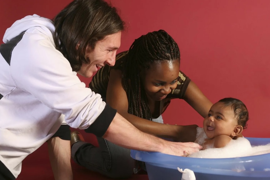 A man and a woman look at a baby in a bath.