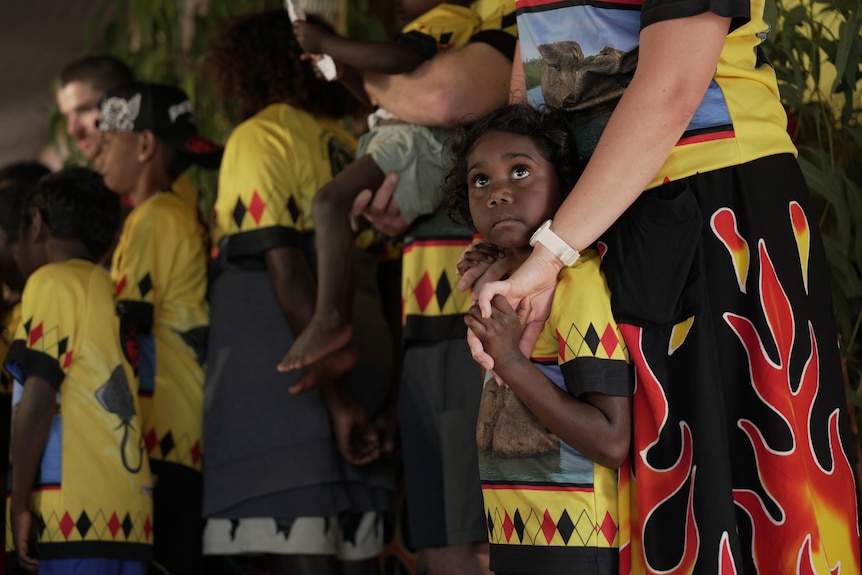 A small boy holds a woman's hand as they stand among a group of people wearing matching outfits.