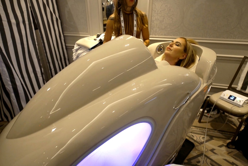 A blonde woman lying in a white pod.