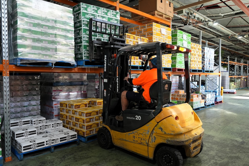 Colourful cardboard cases of beer stacked on shelves. A forklift is moving one pallet load.