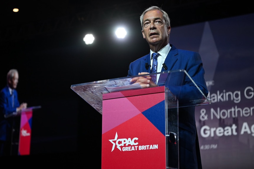 A man at a suit speaking at a lectern.