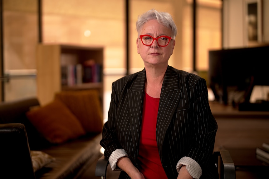 Woman in a red shirt and black jacket and glasses with red frames.