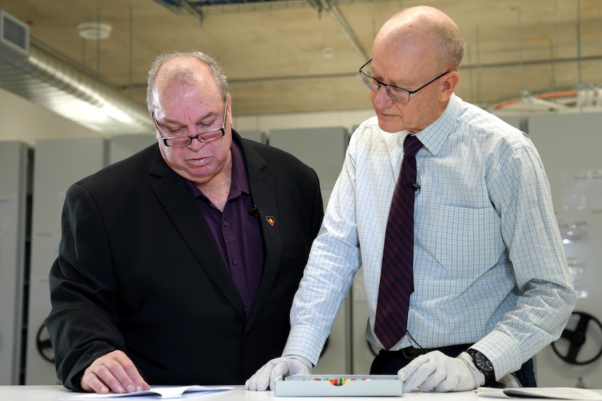 A man wearing a black suit jacket reaches for a file in an archive room.