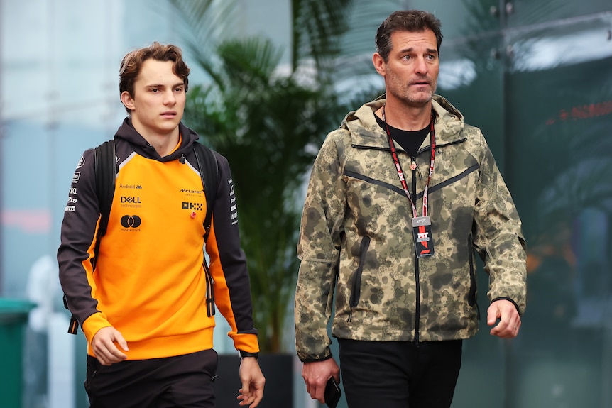 Oscar Piastri of Australia and McLaren and Mark Webber walking in the F1 paddock