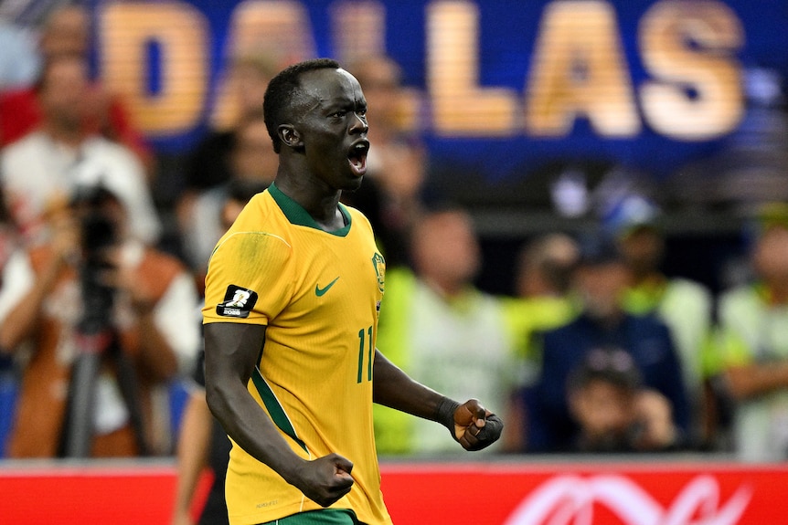 Awer Mabil is wearing a Socceroos shirt, his hands are in fists and he is yelling as he celebrates a penalty score