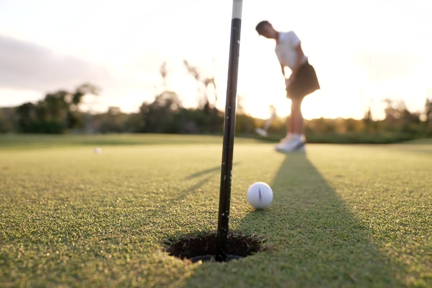 A young girl putts a golf ball on a green.