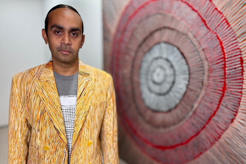 A man in a bright yellow suit stands in front of an artwork with circular shapes.