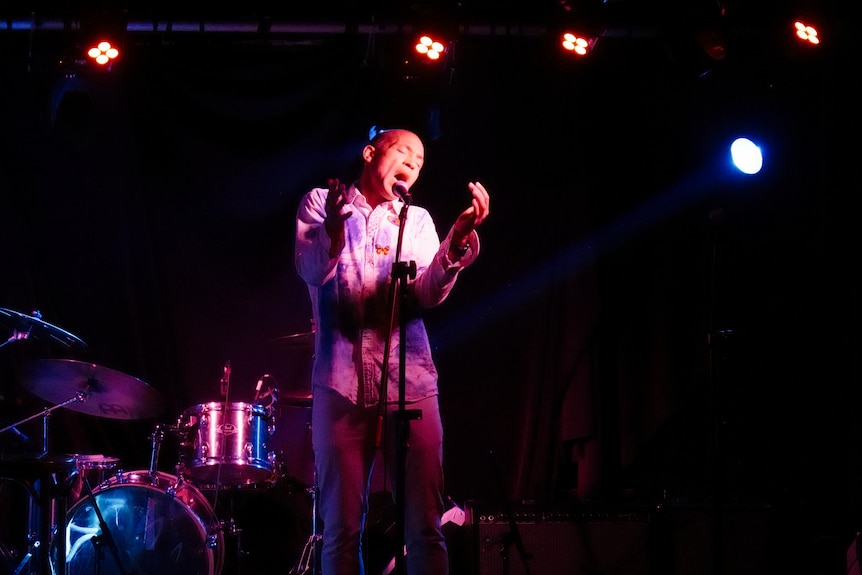A man in his mid fifties performs on stage under a purple spotlight.