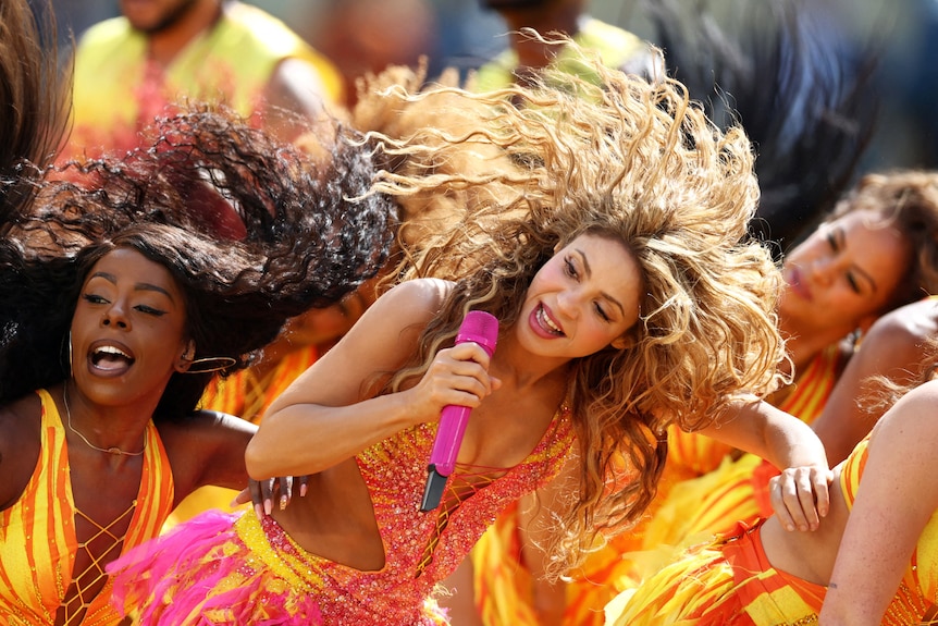 Shakira with hair flowing to one side, mic in hand dancing on stage