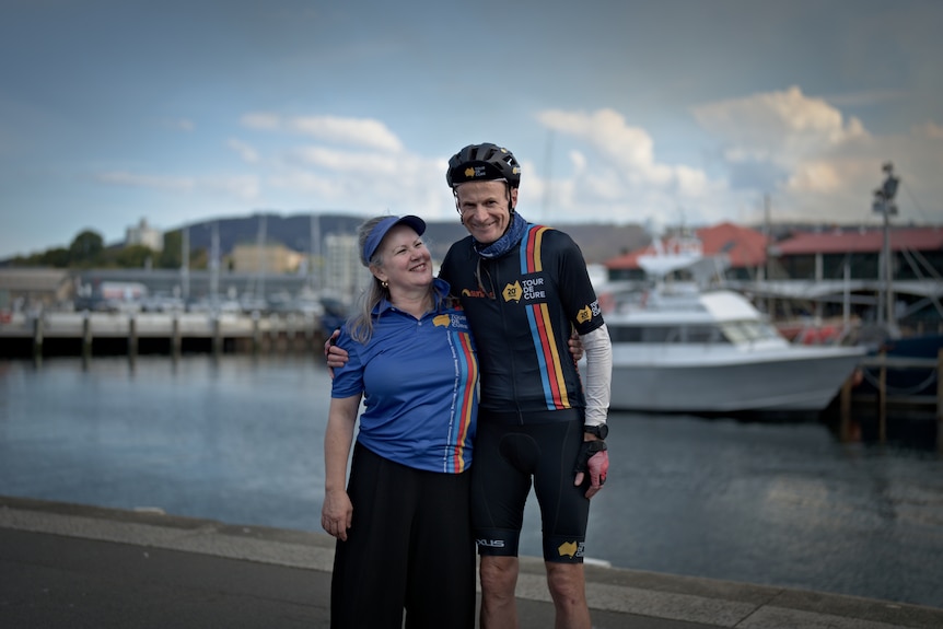 Dr Richard Scolyer wearing biking attire standing in front of the docks in Hobart with his wife