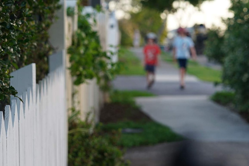 Two anonymous primary school-aged boys walk in distance along a suburban street with houses in Australia.