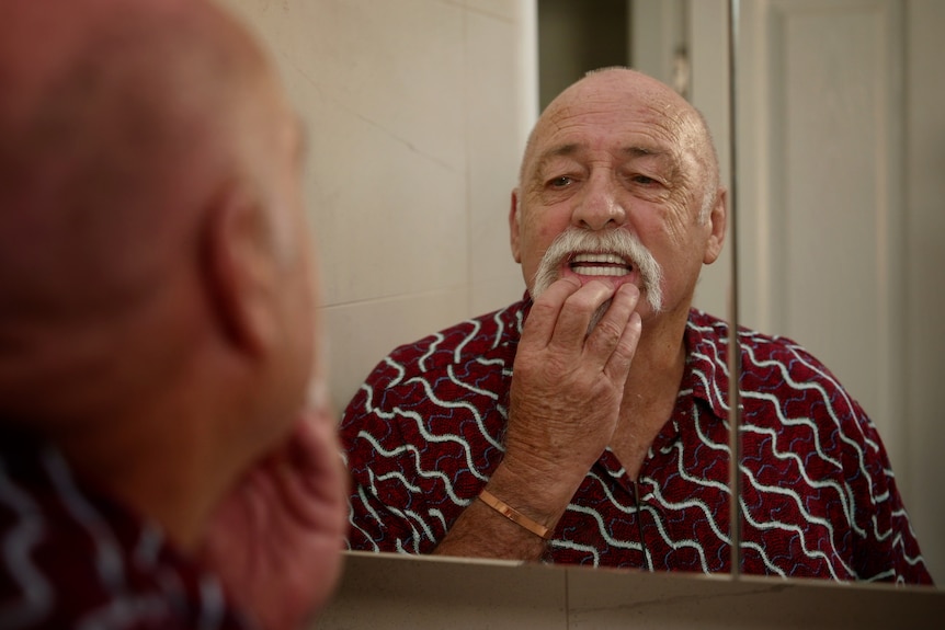 A man examines his teeth in the mirror