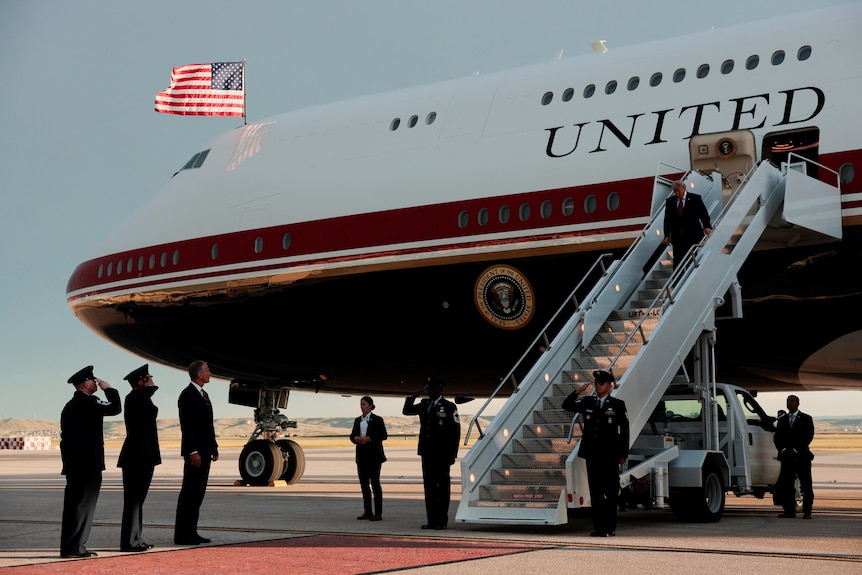 Donald Trump climbs down the stairs of a large jet plane with the US flag on it